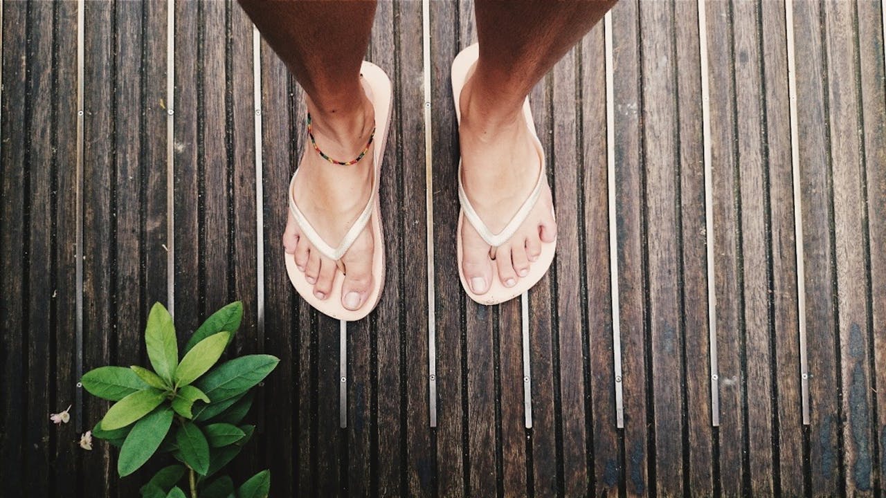 Feet in flip flops on a wooden deck with green leaves, Singapore style.