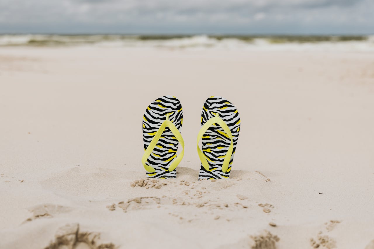 Vibrant zebra print flip flops stand in the sand, capturing summer beach vibes.