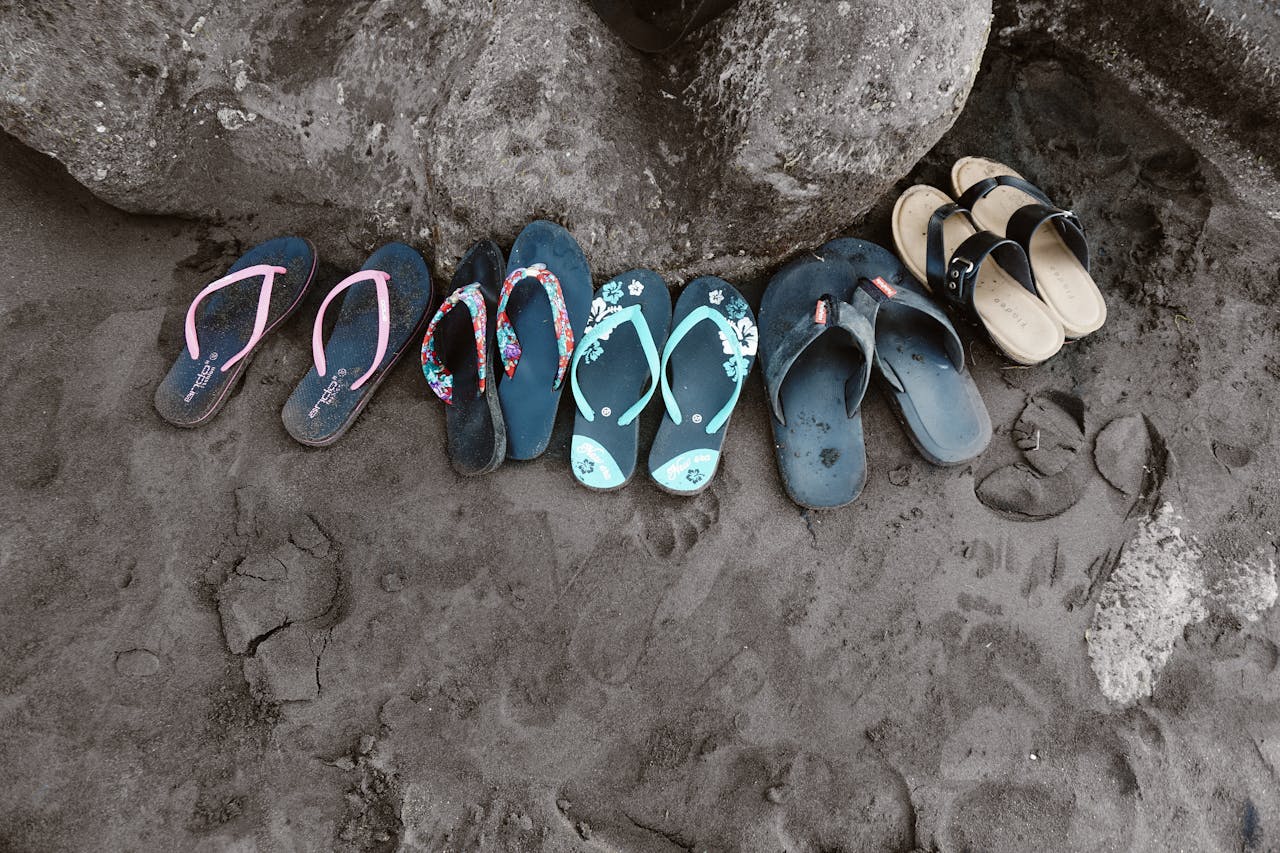 A collection of vibrant flip flops left on the sand in Bali, Indonesia, depicting a casual beach vibe.