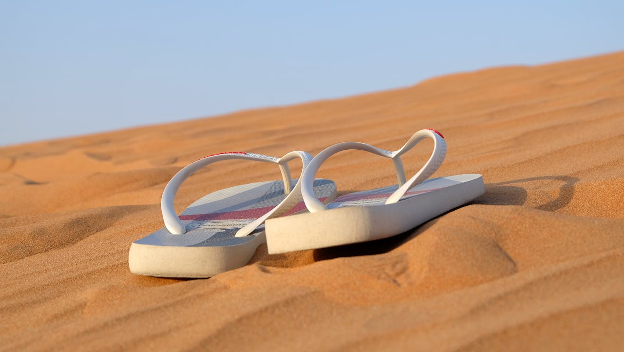 Pair of flip flops placed on sunlit desert sand, symbolizing a summer journey.